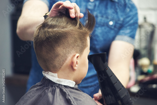 Hairdresser making a hairstyle to a boy in barbershop.