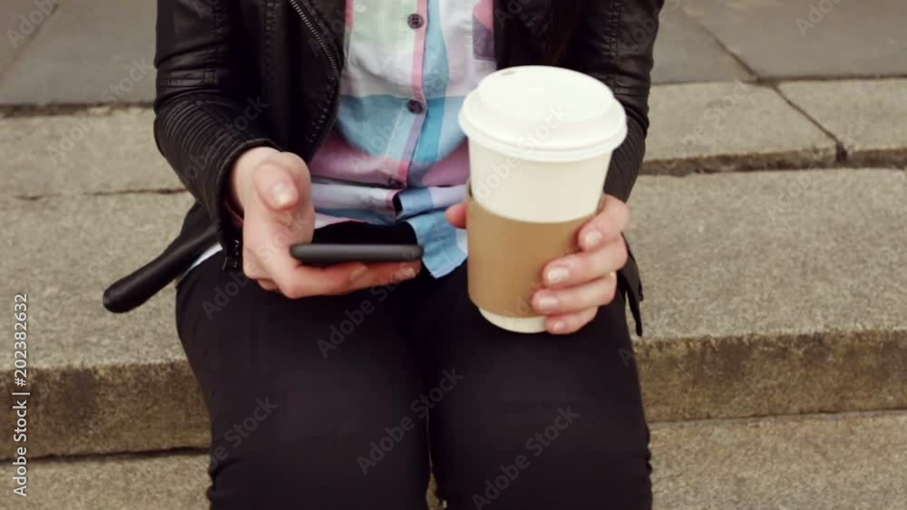 Hands girl close - up, which looks into your smartphone and holds a coffee Hands girl close - up, which looks into your smartphone and holds a coffee