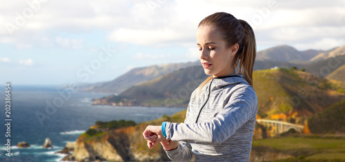 sport, people  and technology concept - woman with fitness tracker training over bixby creek bridge on big sur coast of california background