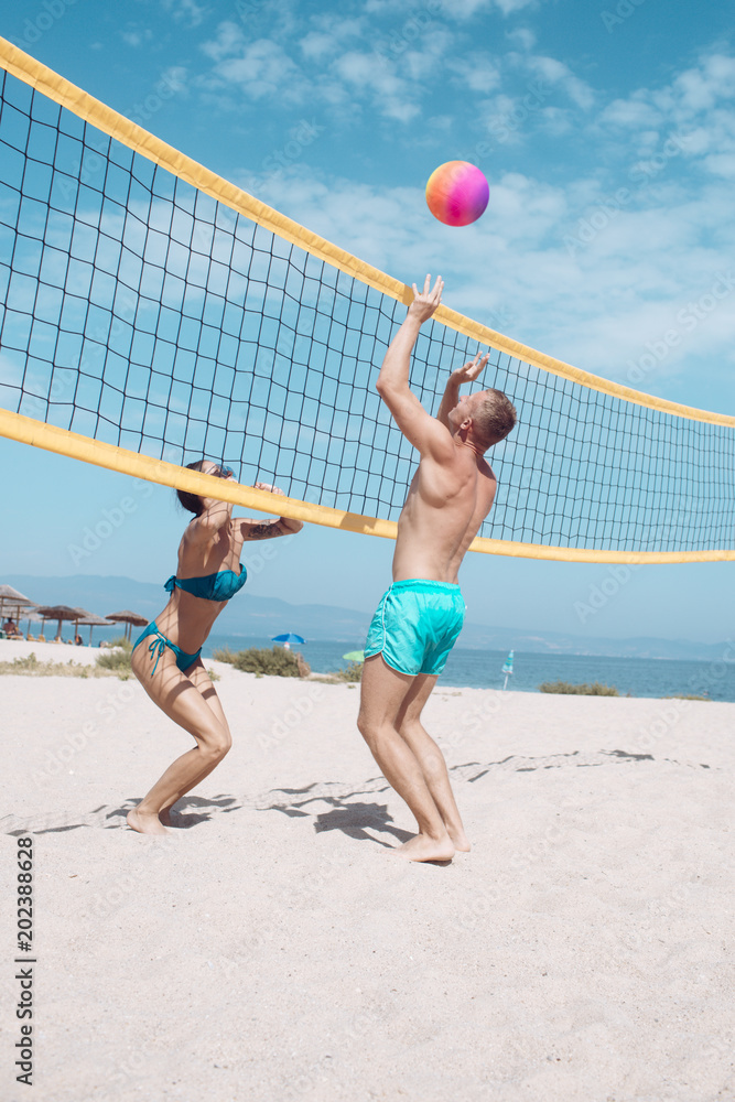 Beach volleyball concept. Couple have fun playing volleyball. Young sporty active couple beat off volley ball, play game on summer day. Woman and man fit, strong, healthy, doing sport on beach.
