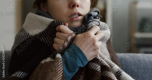 Close up of the young unwell caucasian woman in the warm scarf and a plaid shivering as she having a high temperature. At home. Inside photo