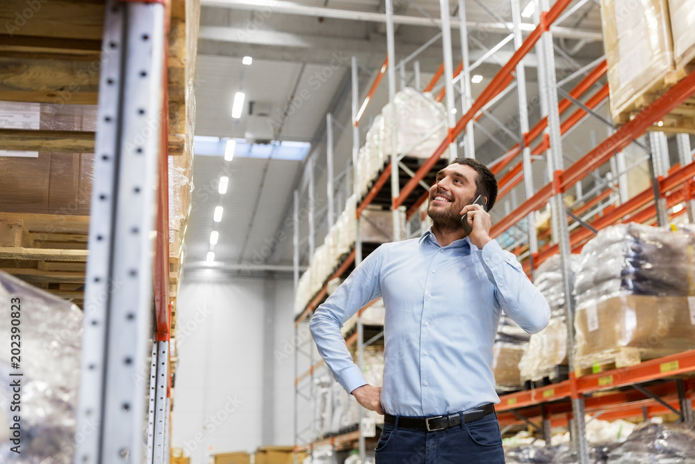 wholesale, logistic business and people concept - smiling businessman calling on smartphone at warehouse