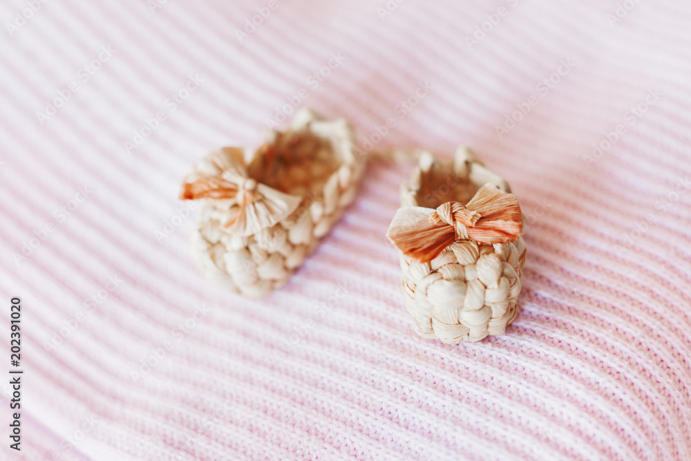 Cute tiny sandals made of straw, ancient traditional russian type of footwear. Natural booties for baby girl with a bow on pink knitted fabric background.