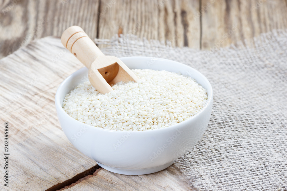 Sesame seeds in a white bowl with a wooden spoon Sesame seeds in a white bowl with a wooden spoon