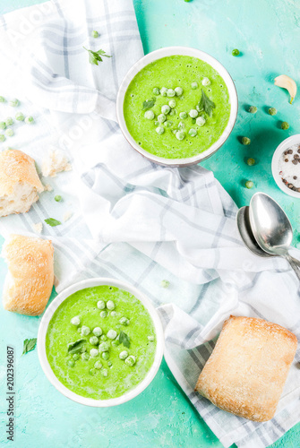 Green pea soup with fresh bread on light blue concrete table, copy space top view