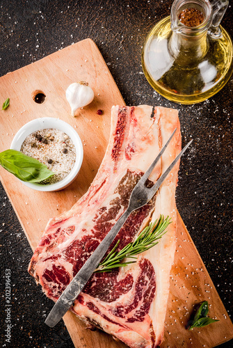 Raw beef marbled meat striplon rib eye steak with spices, herbs, dark background, on cuting board, copy space top view photo