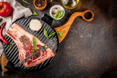 Raw beef marbled meat striplon rib eye steak with spices, grill pan, and herbs, dark background top view, copy space photo