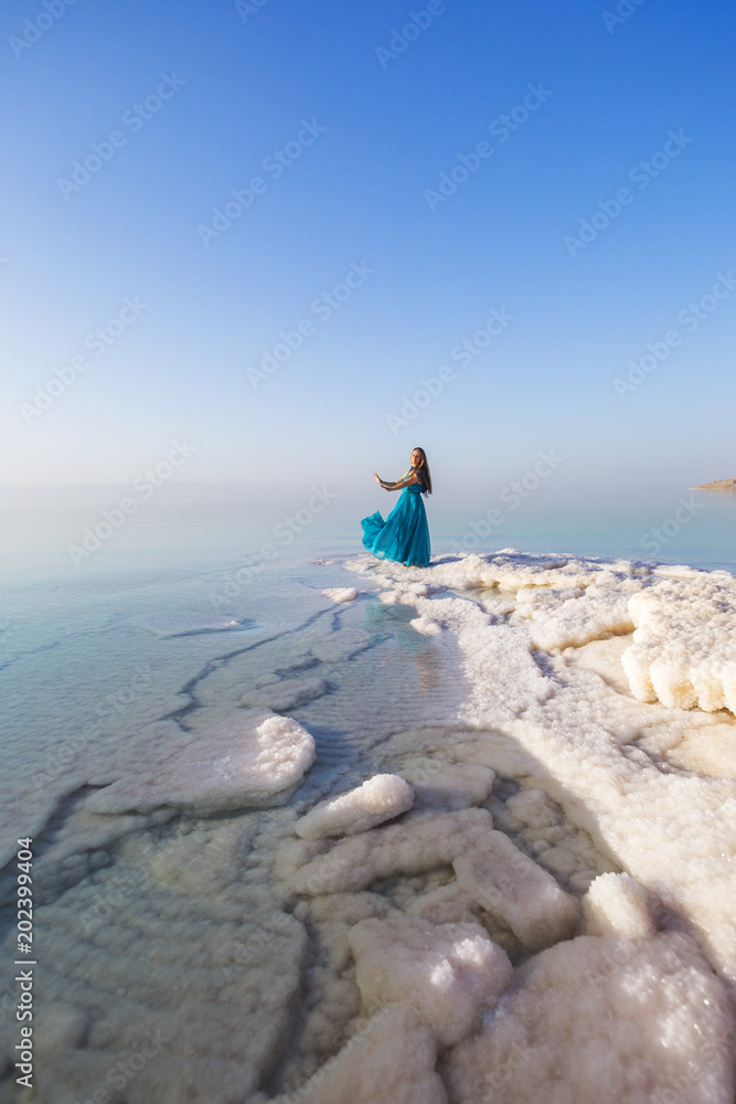 Blonde young girl in a blue dress on the shore of the dead sea. Jordan