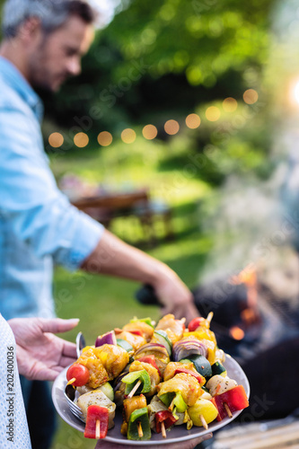 In summer. A couple prepares a bbq to welcome friends in the garden. Close-up on a plate of grill skewers
