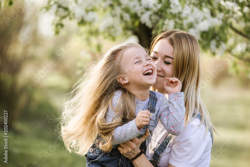 young mother with adorable daughter in park with blossom tree