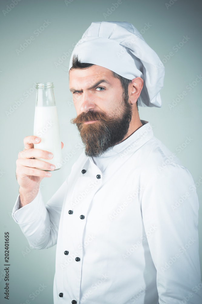 Bearded chef with holds glass bottle. Confident male caucasian cook, confectioner in white coat, hat hold bottle fresh milk for preparing desserts. Baker, confectioner, cook, head-cook, chef with milk Bearded chef with holds glass bottle. Confident male caucasian cook, confectioner in white coat, hat hold bottle fresh milk for preparing desserts. Baker, confectioner, cook, head-cook, chef with milk