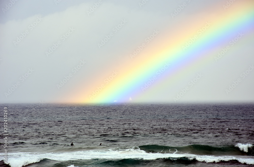 Rainbow over the sea. Seascape with beautiful multicoloured rainbow over the sea. White sailing boat in the background. Rainbow over the sea. Seascape with beautiful multicoloured rainbow over the sea. White sailing boat in the background.