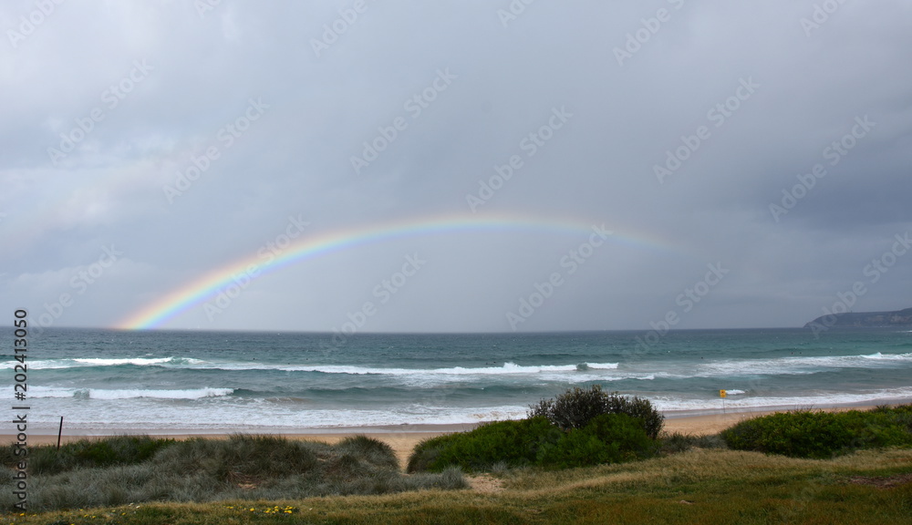 Rainbow over the Tasman sea. Seascape with beautiful multicoloured rainbow over the sea and Curl Curl beach, Australia. Rainbow over the Tasman sea. Seascape with beautiful multicoloured rainbow over the sea and Curl Curl beach, Australia.