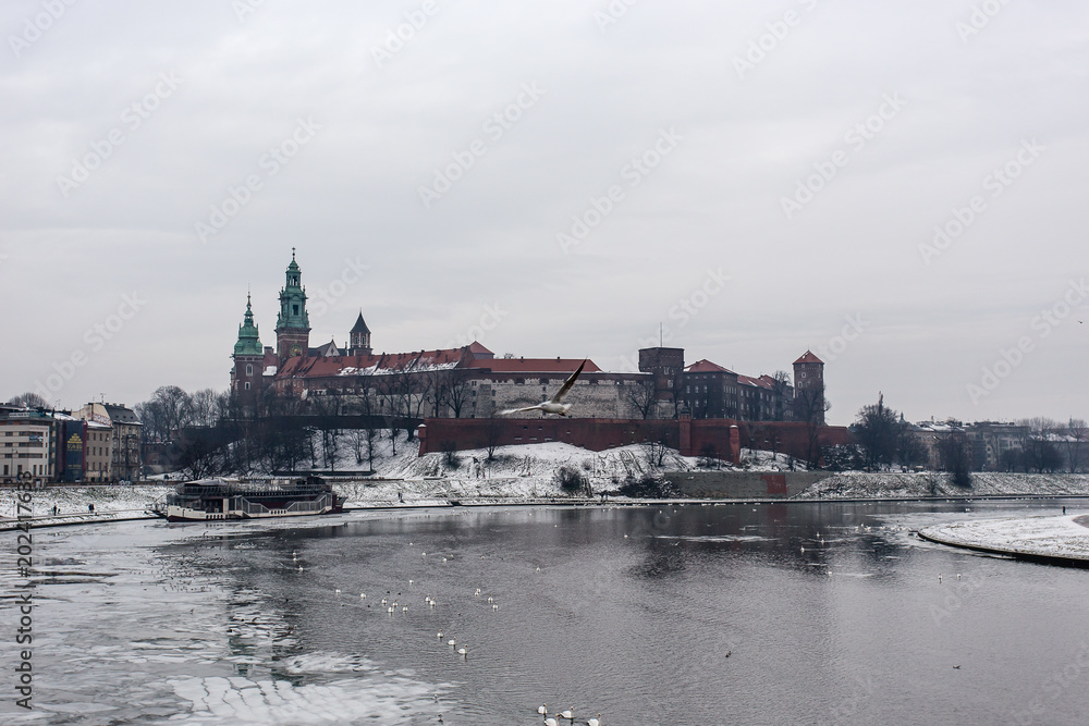 Snowy winter view of Wawel Castle seen from across the Vistula River. Its a cold, cloudy day.Krakow, Poland