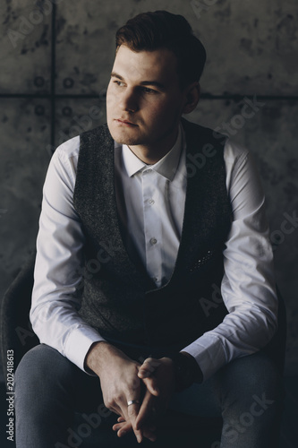 Vertical portrait of a handsome young businessman sitting in a chair and contemplating looking away.
