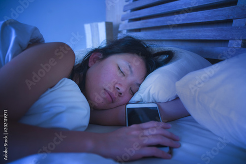 close up portrait of young sweet and beautiful Asian Chinese woman 20s or 30s sleeping in bed next to her mobile phone in internet social media addiction