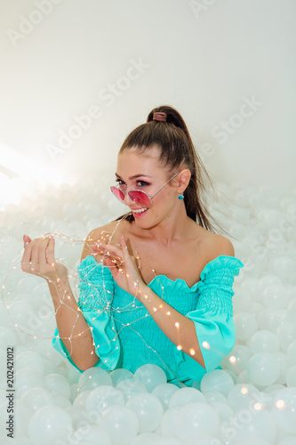 Happy beautiful woman lays surrounded by white plastic balls holding garland photo