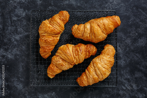 Croissants on a cooling rack on textured dark background  top view.