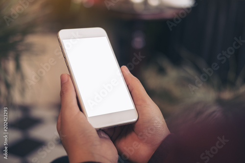 Mockup image of hand holding white mobile phone with blank screen in cafe