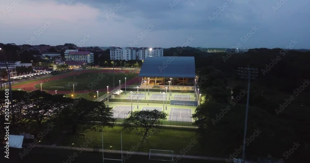 University sports facilities lit up at night by flood lights. Tennis courts, soccer field, basketball. Drone shot at night University sports facilities lit up at night by flood lights. Tennis courts, soccer field, basketball. Drone shot at night