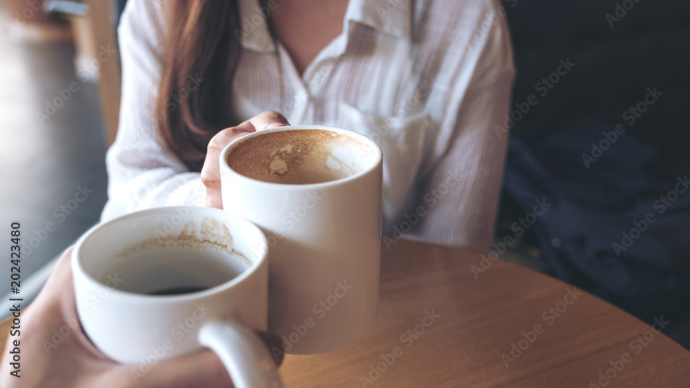 Close up image of a man and a woman clinking white coffee mugs in cafe Close up image of a man and a woman clinking white coffee mugs in cafe