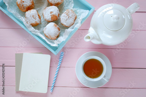Morning tea flat lay. sweet pastries. donuts with powdered sugar in a blue tray,  white kettle and a cup of tea on a pink wooden  background. flat lay in pastel colors. top view, copy space