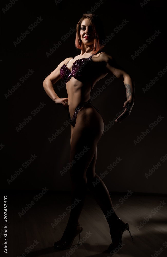 attractive fitness woman, muscles young athlete on dark background