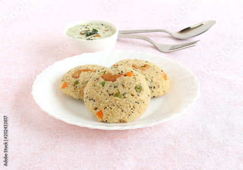 Oats Idli or cake, a healthy Indian vegetarian food, with vegetables like carrot, peas, green beans and capsicum, and cashew nuts, which is steam cooked, and coconut chutney.