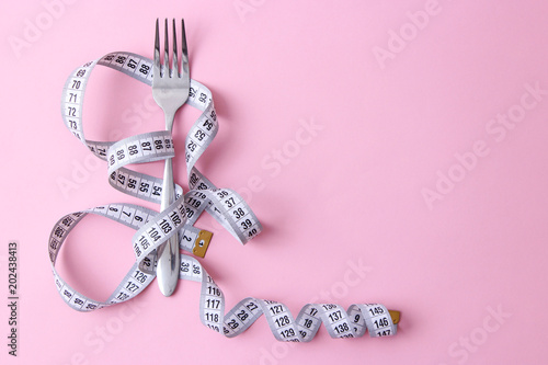 centimeter tape and fork on a colored background with a place for inserting text. composition in the style of minimalism. concept of health, weight loss, diet, proper nutrition. 