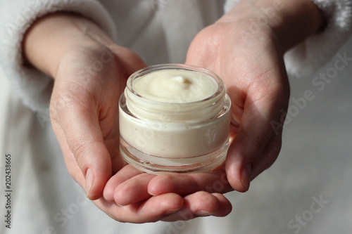 a girl in a bathrobe holds a jar with a cosmetic cream in her hands. skin care, minimalism. keep youth and skin elasticity.  