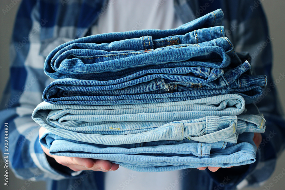 A pile of jeans in men's hands on a light background. the seller in a  clothing store Stock Photo | Adobe Stock
