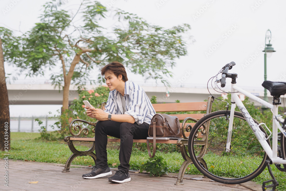 Young man using phone while sitting on bench with bicycle in park Young man using phone while sitting on bench with bicycle in park
