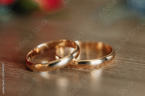 Beautiful picture with wedding rings lie on a wooden surface against the background of a bouquet of flowers