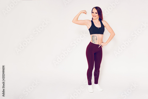 Fototapeta Naklejka Na Ścianę i Meble -  fitness girl is standing on a white background and smiling showing her bicep