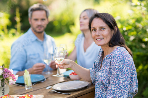 A bunch of friends gathered to share a meal around a table in the garden. Focus on a beautiful woman looking at the camera
