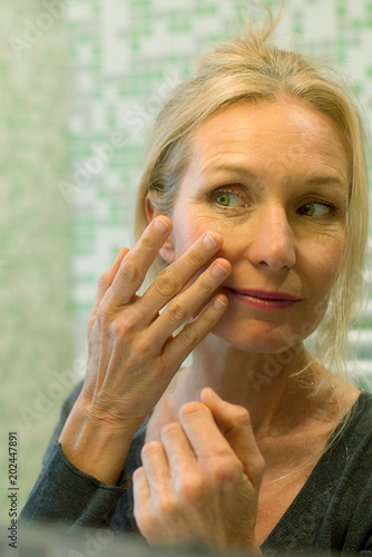 Mature woman scrutinizing her face in bathroom mirror