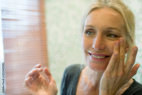 Mature woman looking at her reflection in mirror with hands on cheeks