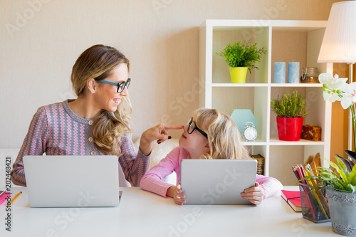 Mother and daughter sitting at table and using computers together