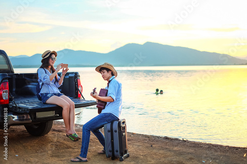 couple traveler playing guitar and watching sunset near the lake background  the mountain.Asia tourist enjoying for sunset during holiday © Anusorn