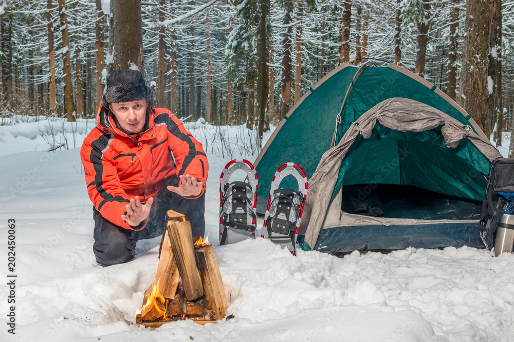 Φωτογραφία a frozen lost tourist near a tent warms his hands by the fire