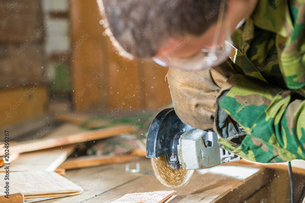 carpenter in goggles processes the surface of the boards with a tool