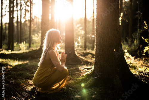 Junge Frau betet im Wald zum Sonnenuntergang
