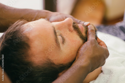 Young bearded man getting face tratment at beauty salon
