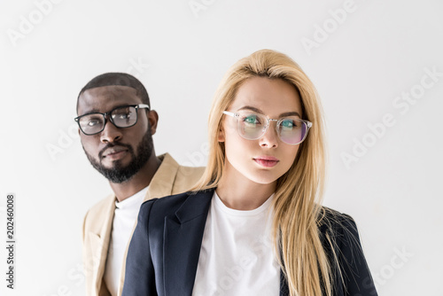 portrait of beautiful stylish young multiethnic couple in spectacles looking at camera isolated on grey