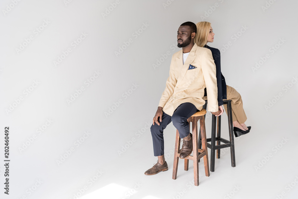 high angle view of fashionable young multiethnic couple sitting back to back on grey high angle view of fashionable young multiethnic couple sitting back to back on grey