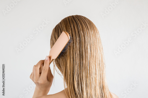Young woman with comb brushing her wet, blonde, perfect hair after shower on the gray background. Care about beautiful, healthy and clean hair. Beauty salon concept. Back view.