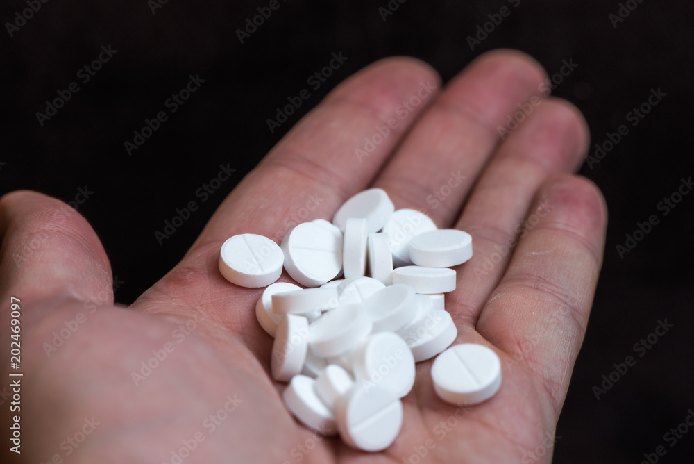White pills in hand on black background closeup White pills in hand on black background closeup