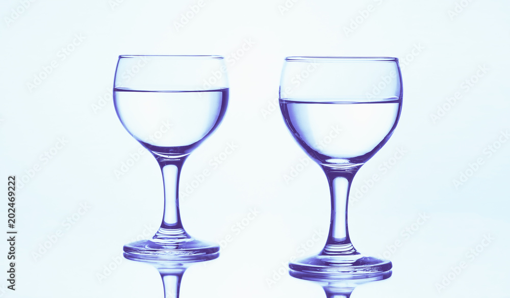Two stemmed glasses of water isolated on a white background with mirror reflection.