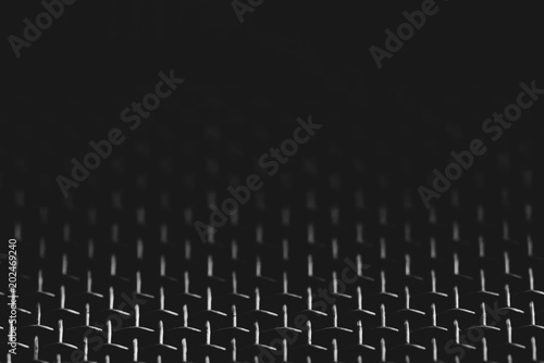 Background image of shiny mesh on dark backdrop. Metallic texture of grid close-up. Triangular shape of grid. Abstract image of surface of audio speaker in macro photography. Futuristic design. © Daniil
