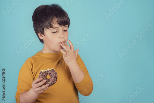 Fotografie niño comiendo una rosquilla de chocolate sobre fondo azul